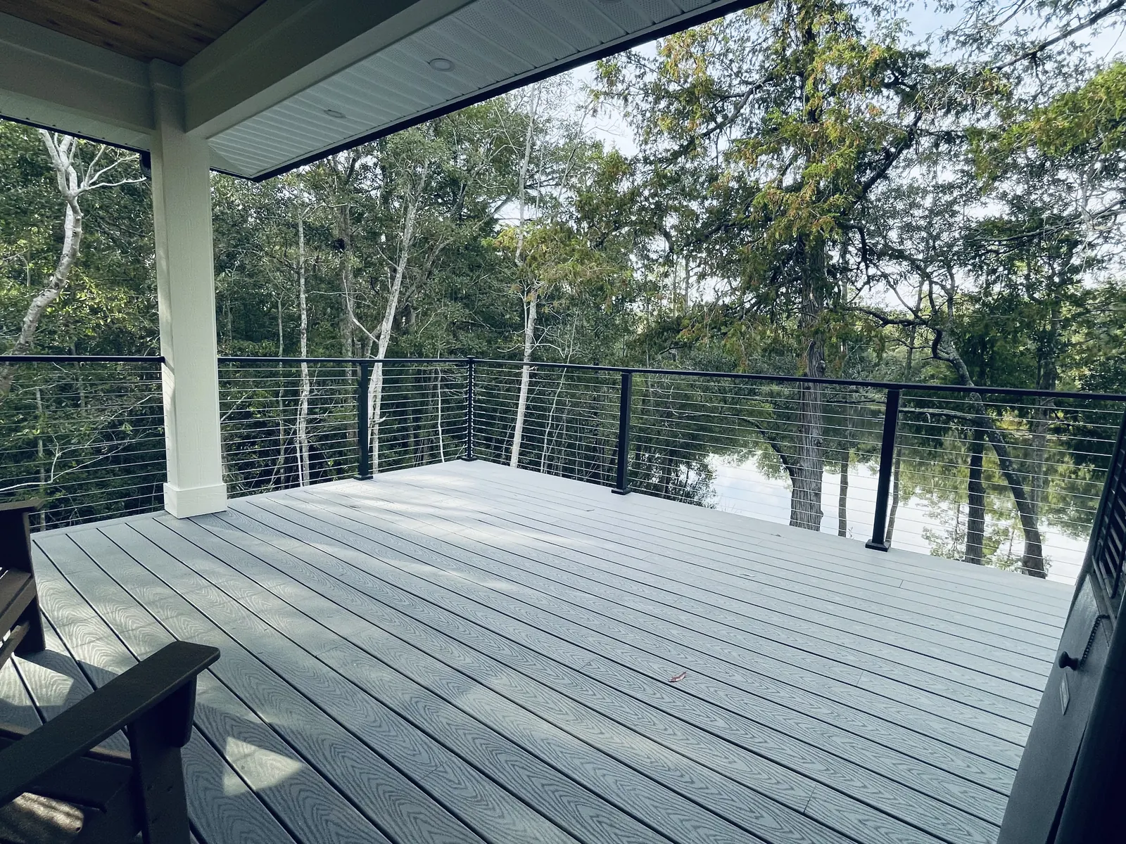 Covered deck with stainless cable railing on black posts looking over the water