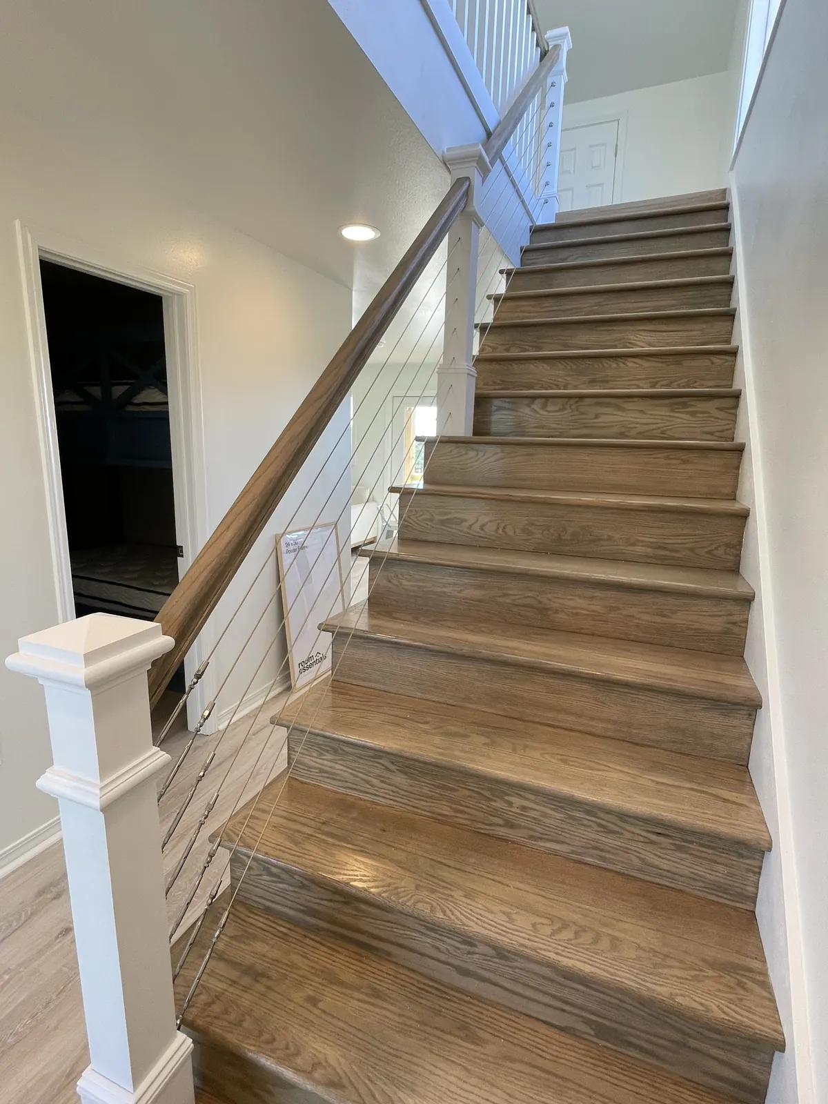 Interior wood staircase with a white newel post and cable railing