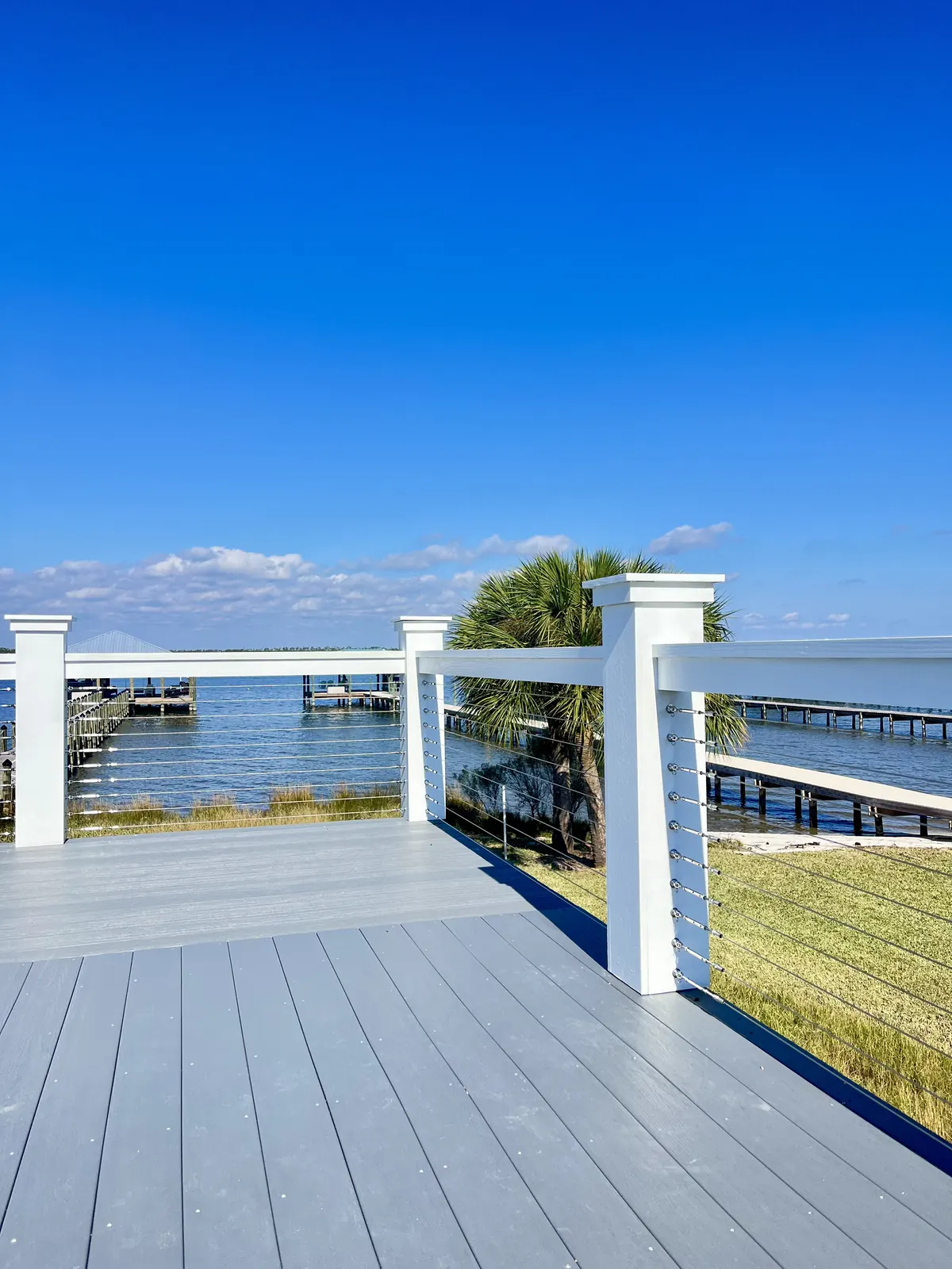 Gray composite deck with white posts and stainless cable railing facing the bay