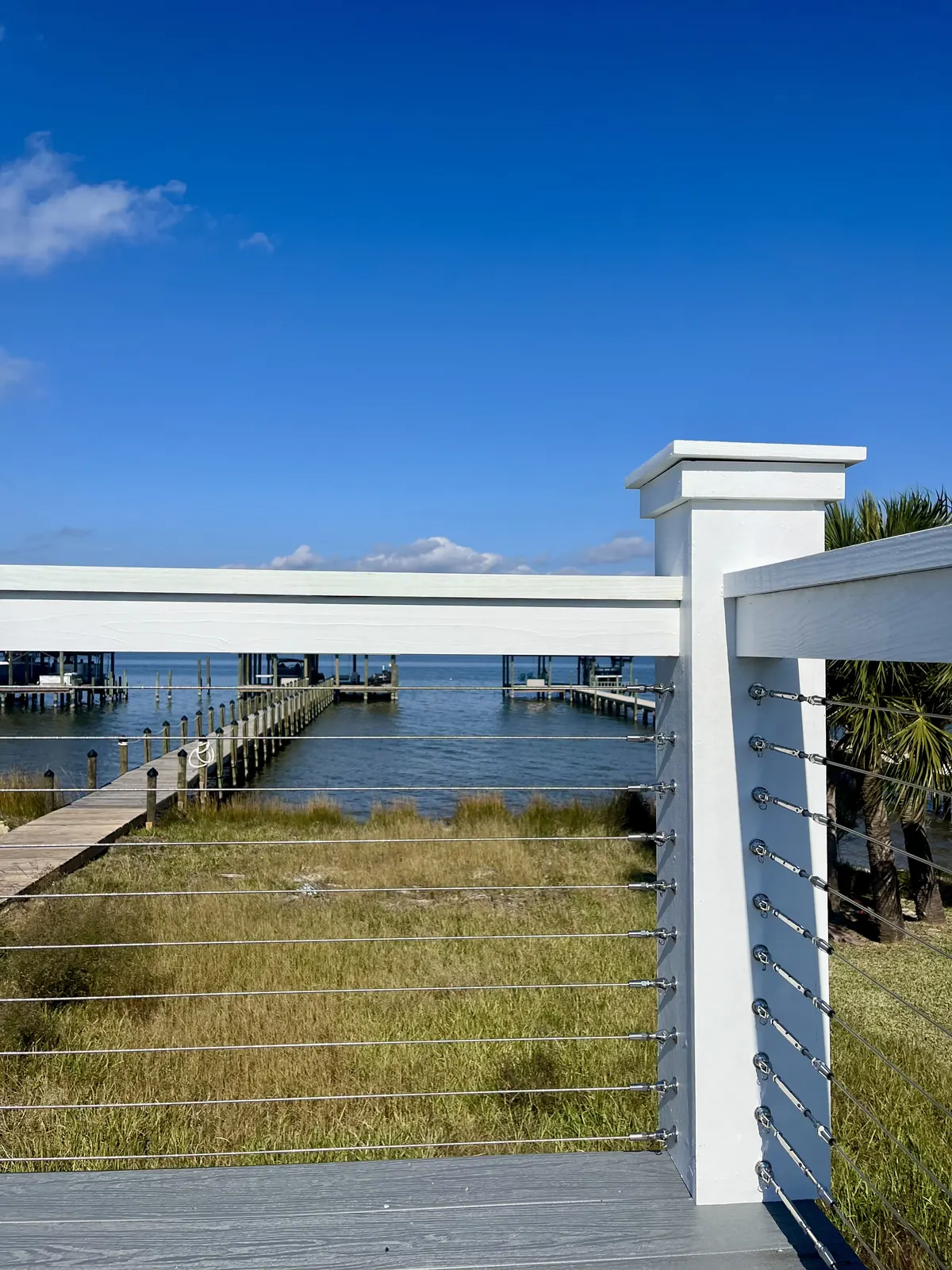 White corner post with stainless cable runs overlooking a boardwalk and pier