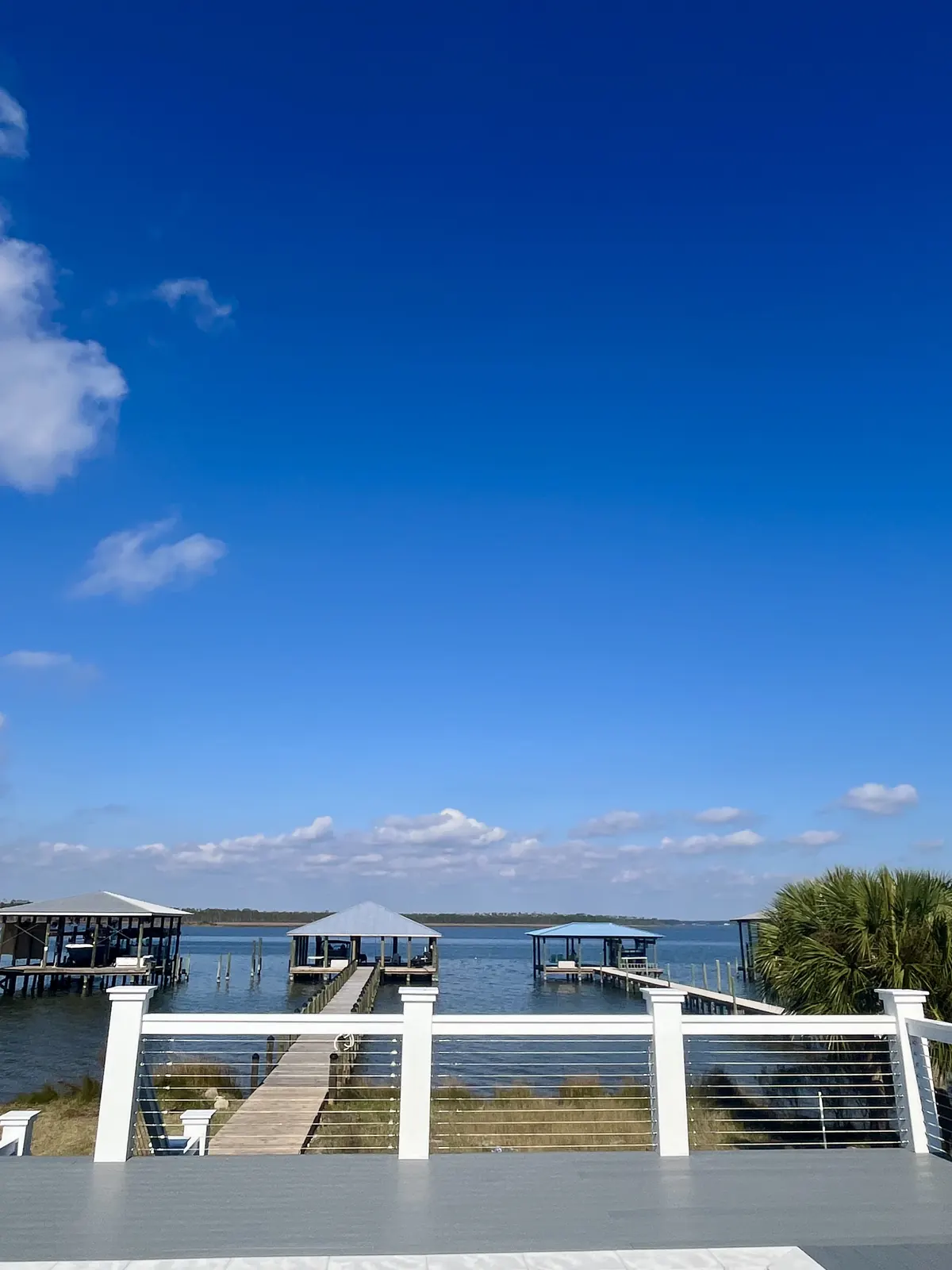 Stainless cable railing between white posts with boathouses on the water behind