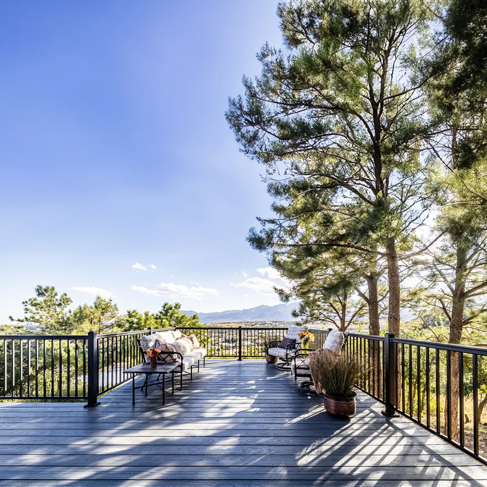 Composite deck with black aluminum railing among tall pines