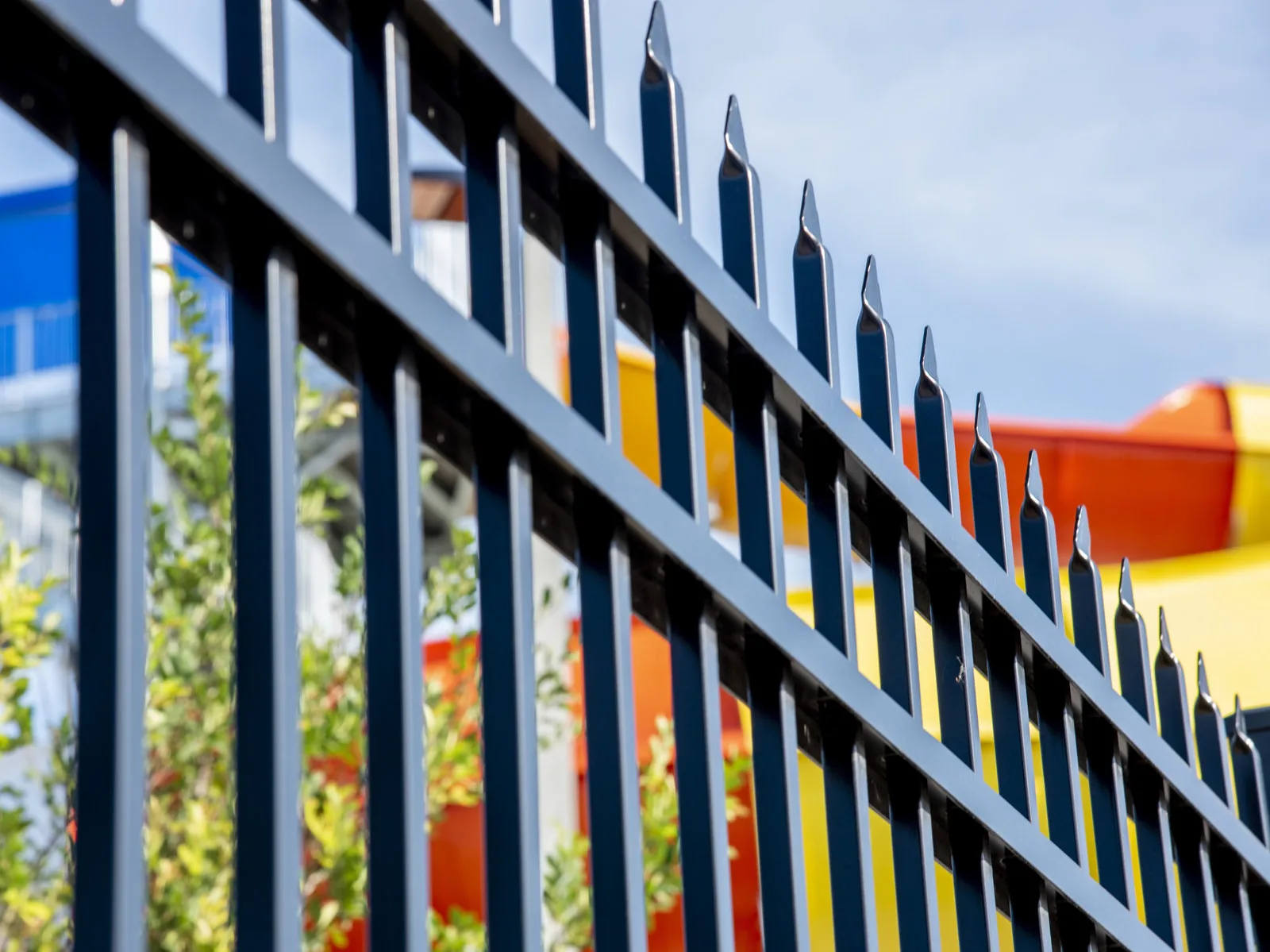 Black aluminum spear-top fence panel close-up against blue sky