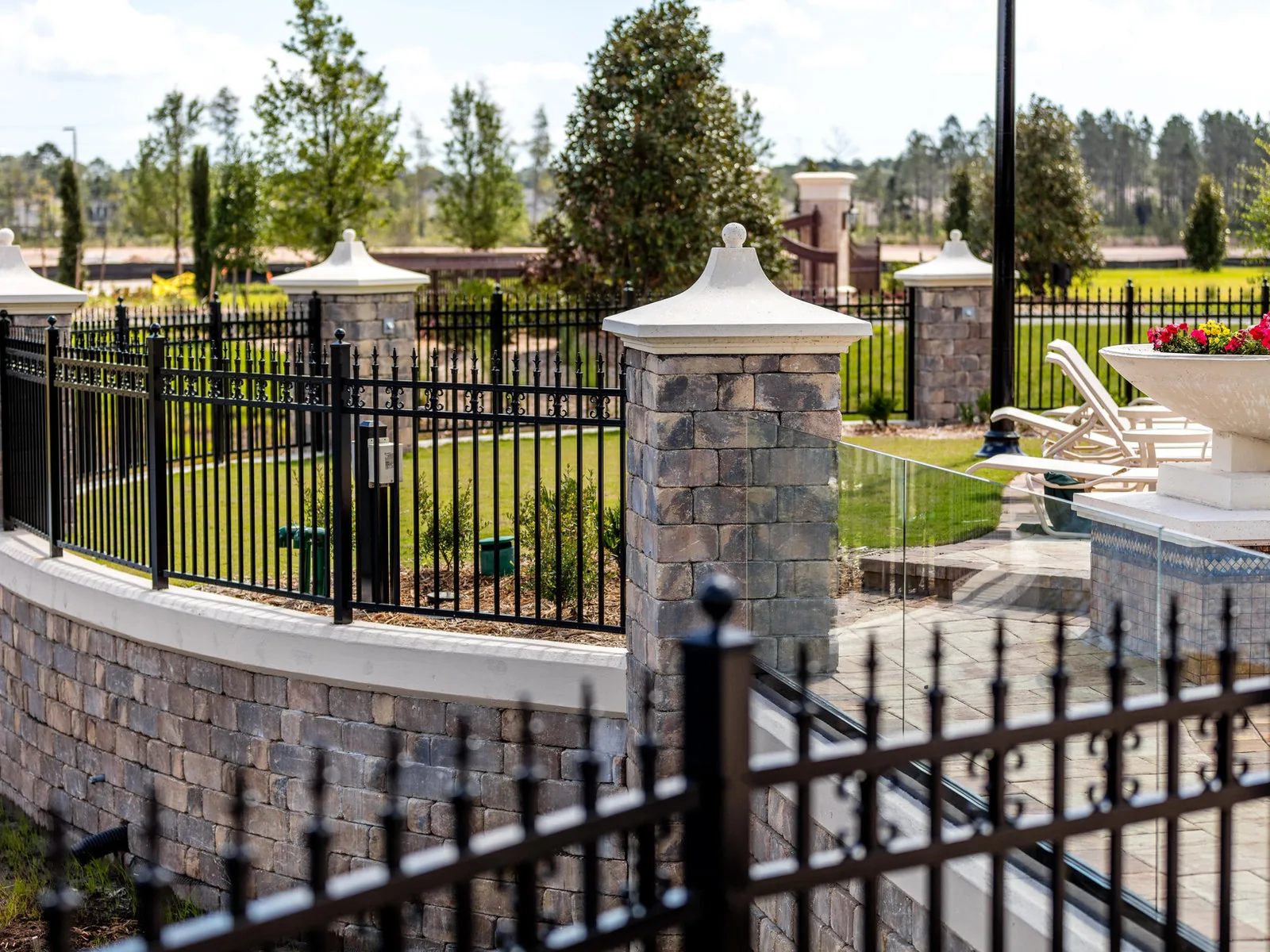Black aluminum fence panels set between stone pillars and a curved stone wall