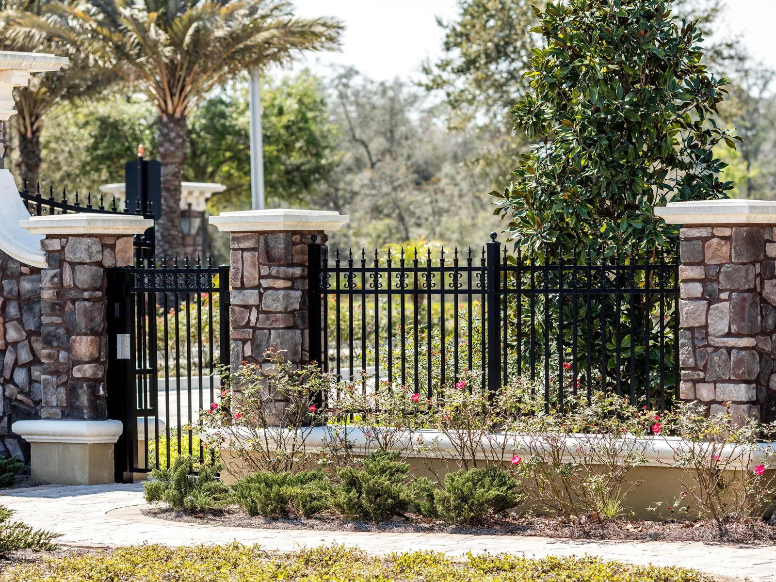 Black aluminum fence and gate between stone pillars at a community entrance
