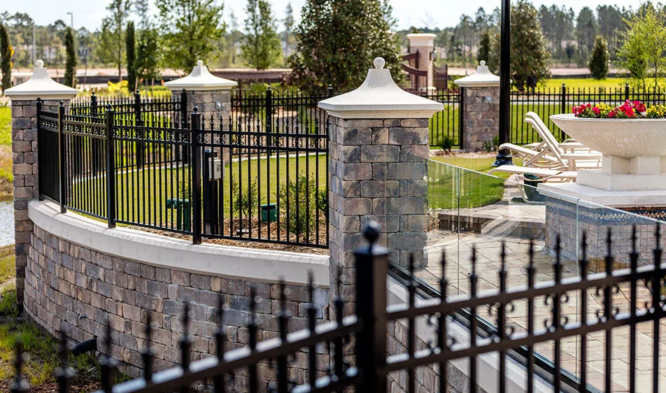 Black aluminum fence and gate with stone pillars and a landscaped wall