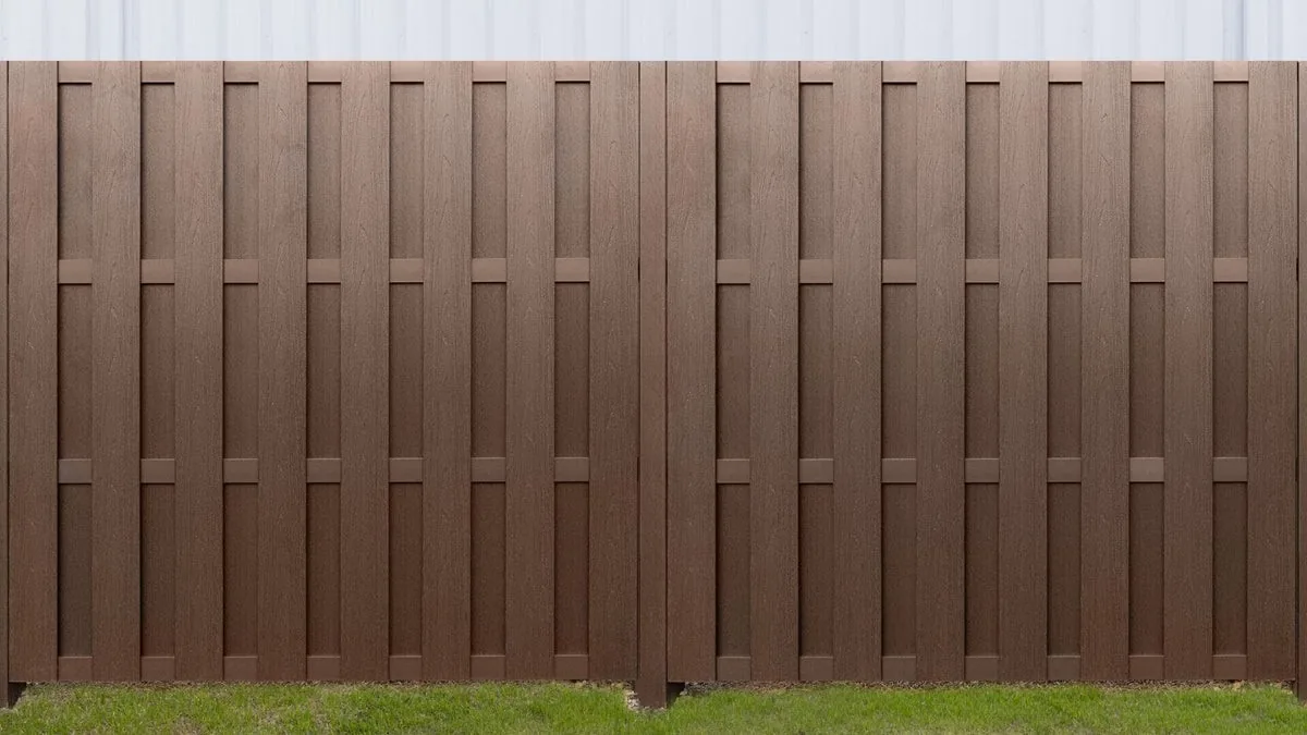 Brown cap composite shadowbox picket fence beside a metal building