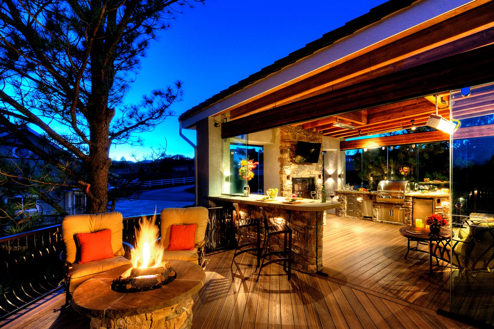 Covered deck with an outdoor kitchen and fire table at twilight