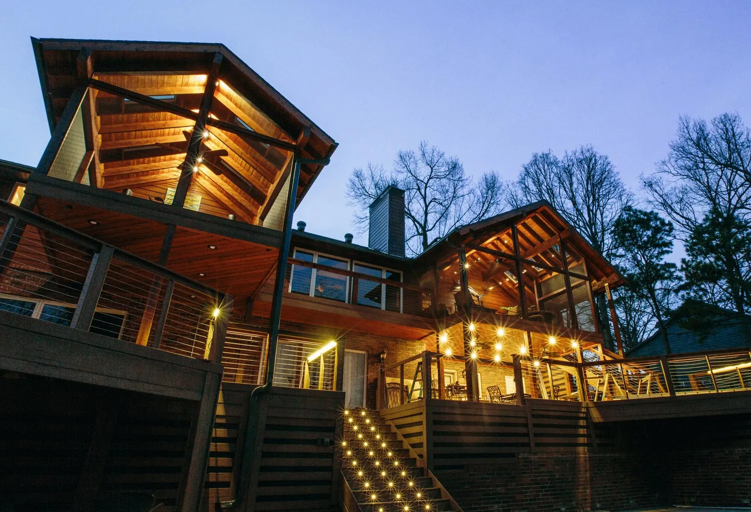 Lakeside home with lit multi-level decks at dusk