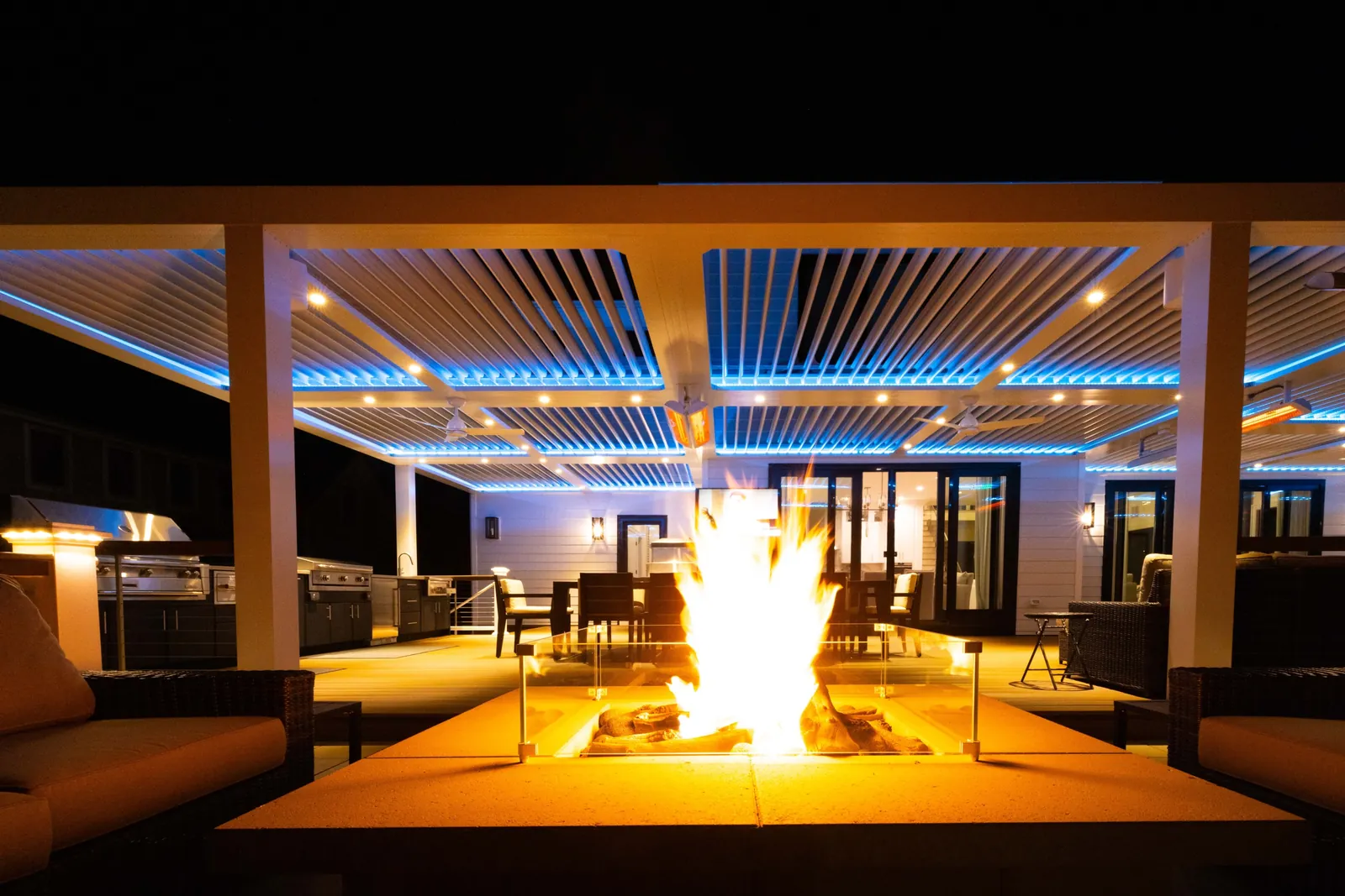 Louvered pergola glowing over a fire pit and outdoor living room at night