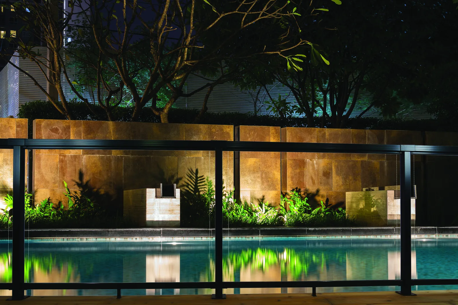 Glass railing by a lit pool at night