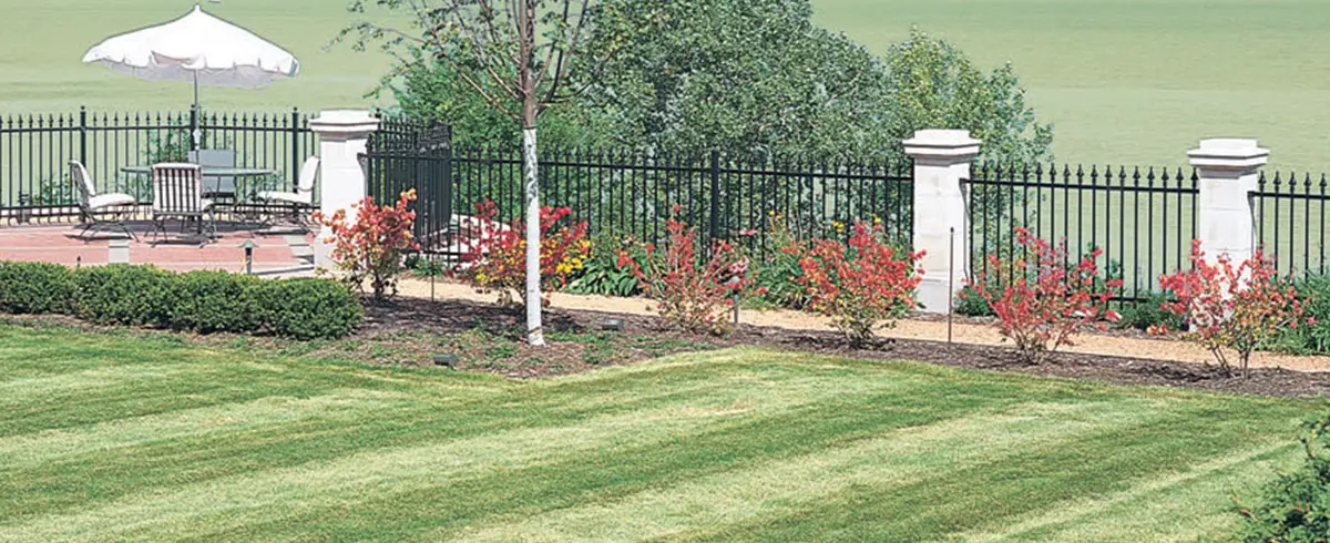 Black ornamental steel fence with white pillars along a lawn