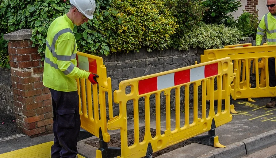 Worker setting up yellow Avalon plastic barriers on a pavement