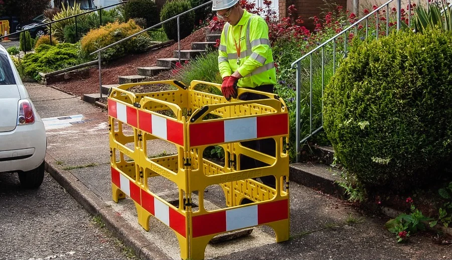 Worker placing yellow and red Oxford SafeGate barriers around a pavement hole